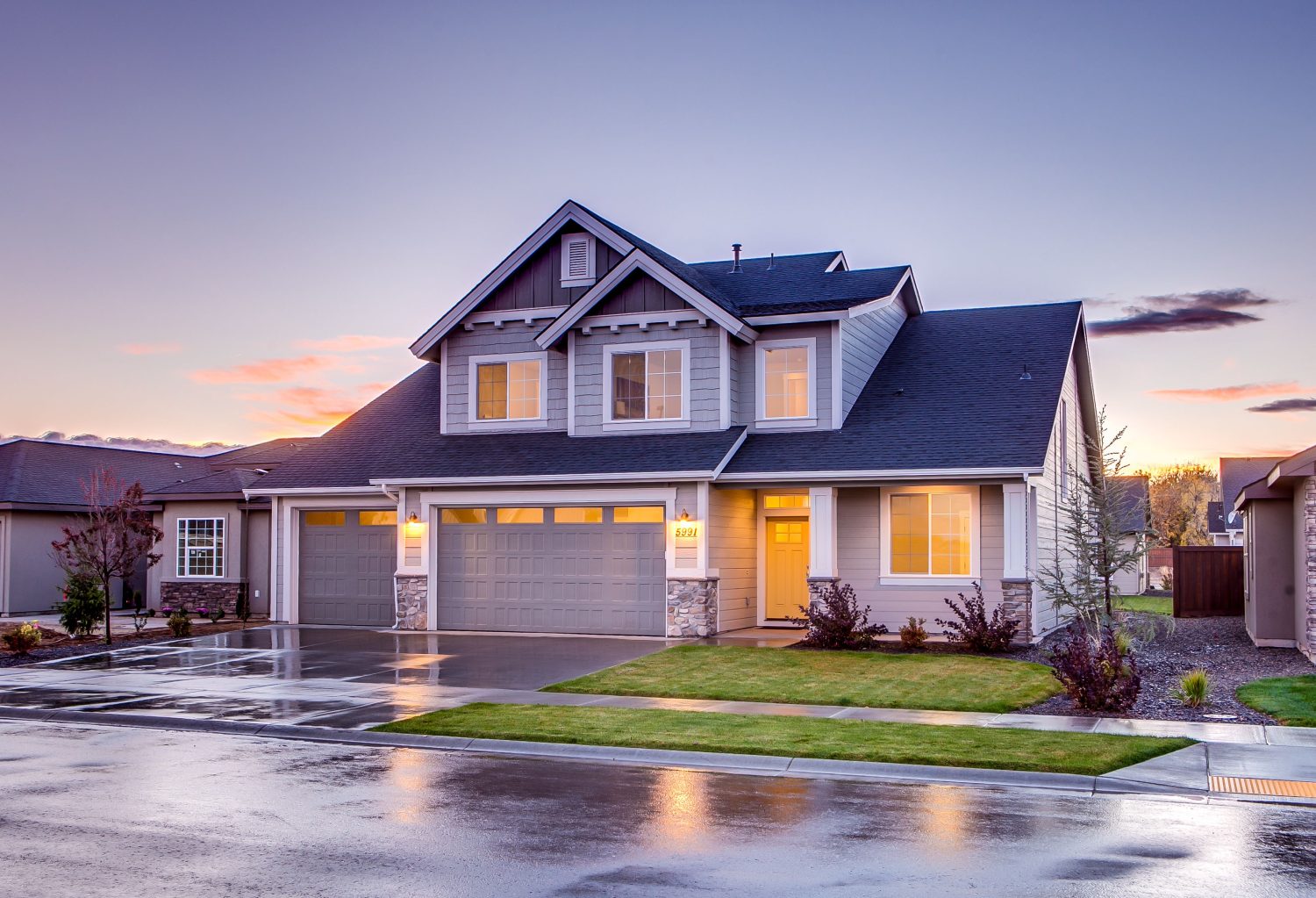 A two-storey family home with its windows lit at dusk